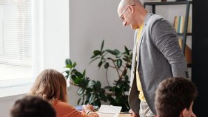 Teacher assisting students in a bright classroom setting.